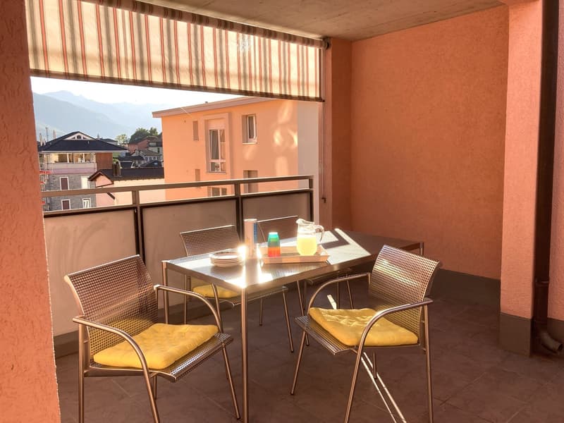 balcony, metal table with chairs, large panoramic windows, retractable sunshade, distant mountain view