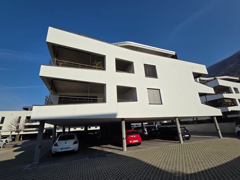 White residential building with multiple balconies and covered parking area