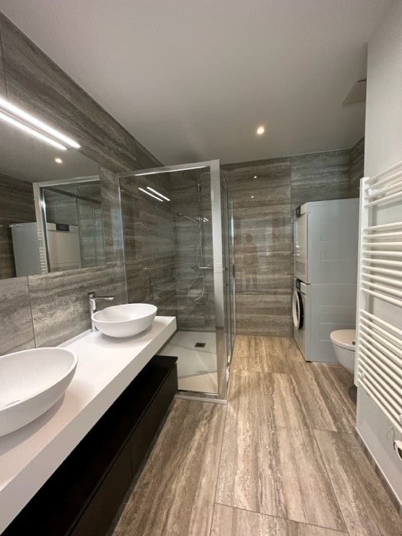 wooden flooring, 2 sinks, a shower, washing machine, mirror, towel rack