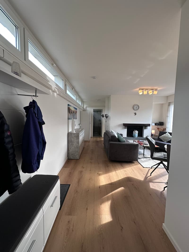 Living room with fireplace, grey couch, carpet, large window, desk, armchair, and table