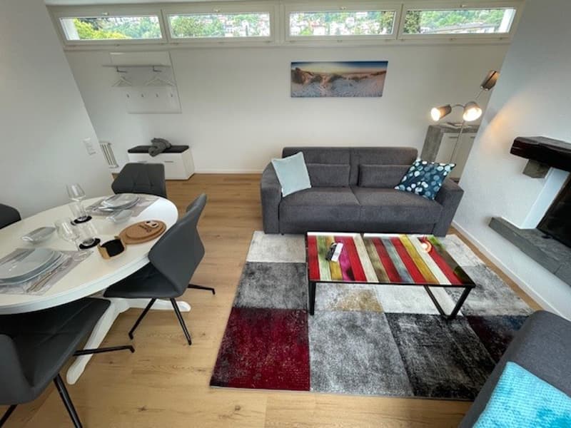 Wooden floor, gray sofa, multicolored rug, dining table, four chairs, fireplace, table lamps
