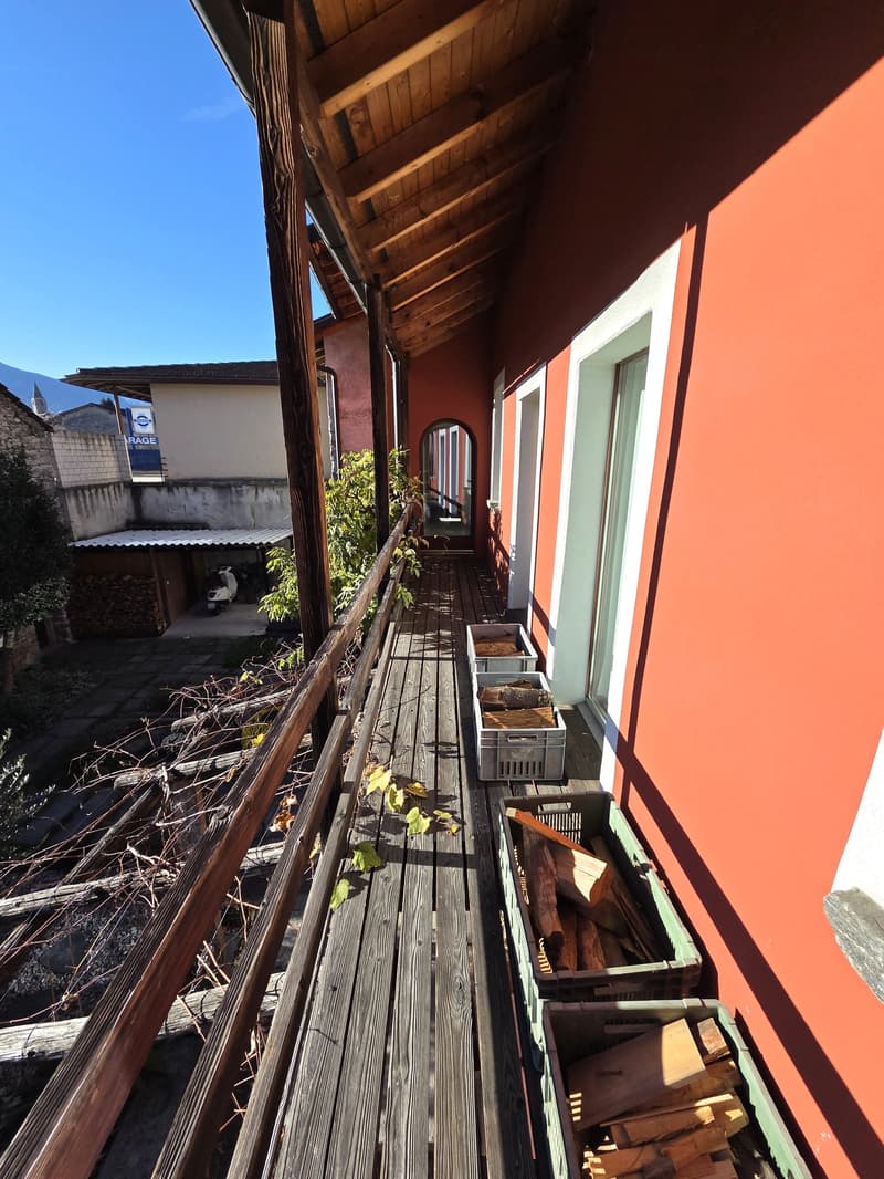 Terraced balcony with wooden floor and railing, open view, plants, and a motorcycle parked in a garage