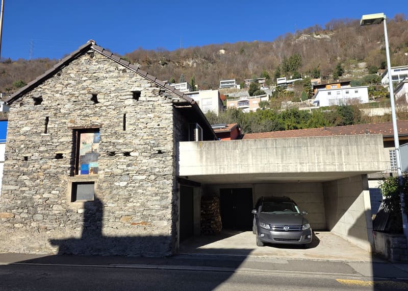 stone wall building, car parked in garage, trees in the background