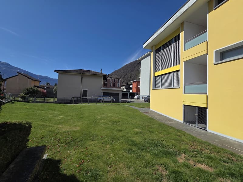 Yellow building with multiple windows, a grassy lawn in front, and a mountain in the background.