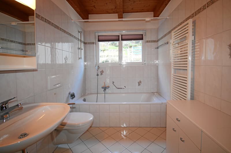 A modern bathroom with white tiles, a bathtub, a sink, a toilet, a mirror, and a wooden ceiling.