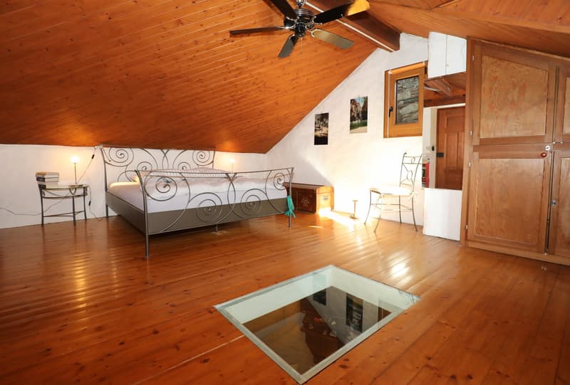 Spacious attic bedroom with wooden ceiling and floor, metal bed frame with decorative design, side table, and glass-topped coffee table