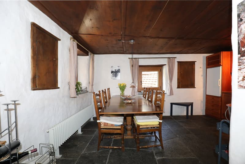 Rustic dining room with wooden ceiling, white walls, large wooden dining table and chairs, curtains, and a fireplace visible.