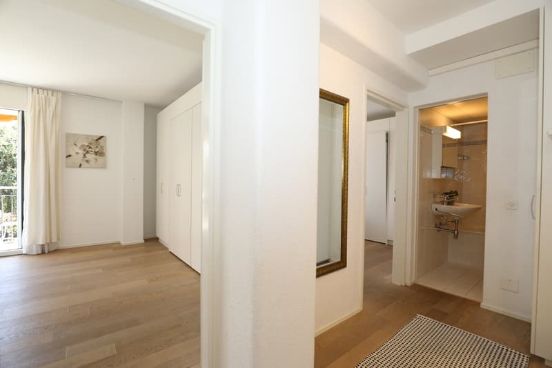 Empty room with wooden floor, white walls, large mirror, and a balcony with a view