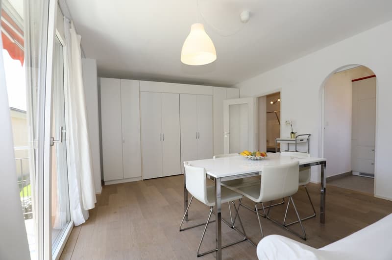Dining room with white table and chairs, white cabinets, glass door, wooden floor, white walls, pendant light