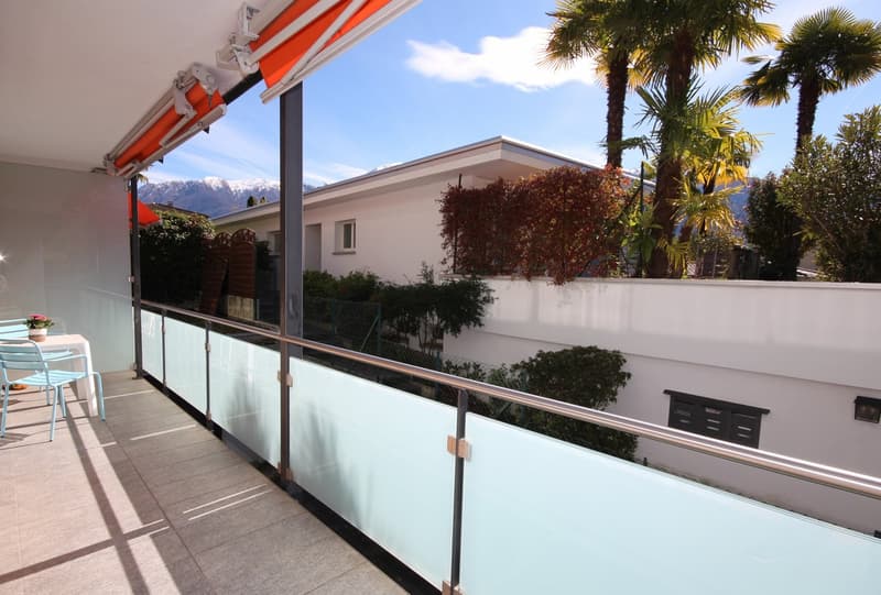 Balcony with glass railing, table and chairs, potted plant, view of mountains
