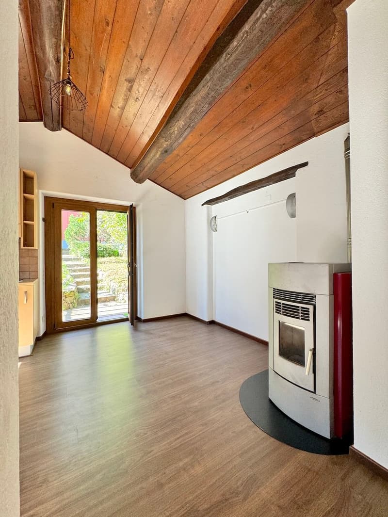 This image shows a room with a wooden vaulted ceiling, hardwood floors, and a fireplace. The room has a large window that provides natural light and a view of the outdoors. The room appears to be a living or family room, with a cozy and rustic feel.