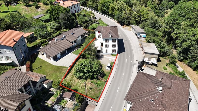 Aerial view of a residential area with multiple houses, a road running through the middle, and a large open space or lot highlighted by the red outline
