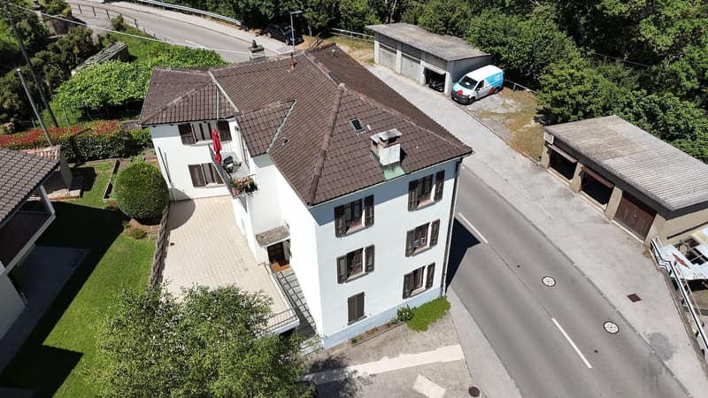 3-story apartment building with brown tiled roof, white exterior walls, and multiple windows. There is a van parked in the driveway next to the building.