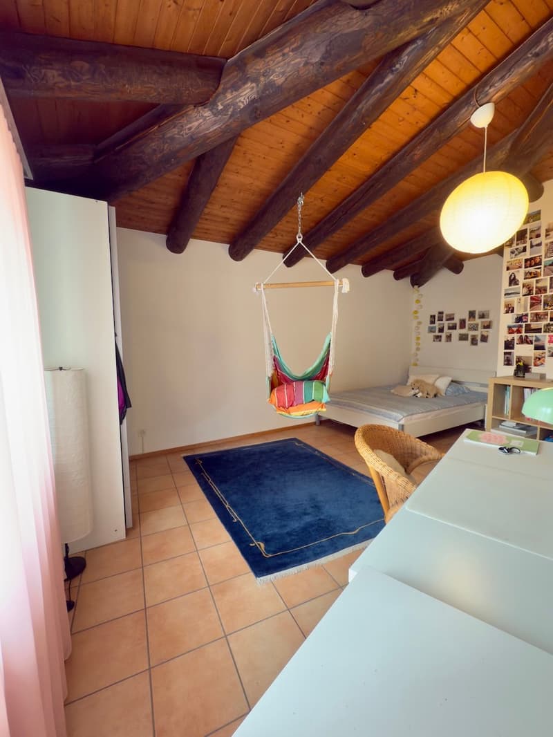 Cozy attic room with wooden beams, a hammock chair, a blue rug, and a wall covered with photos.