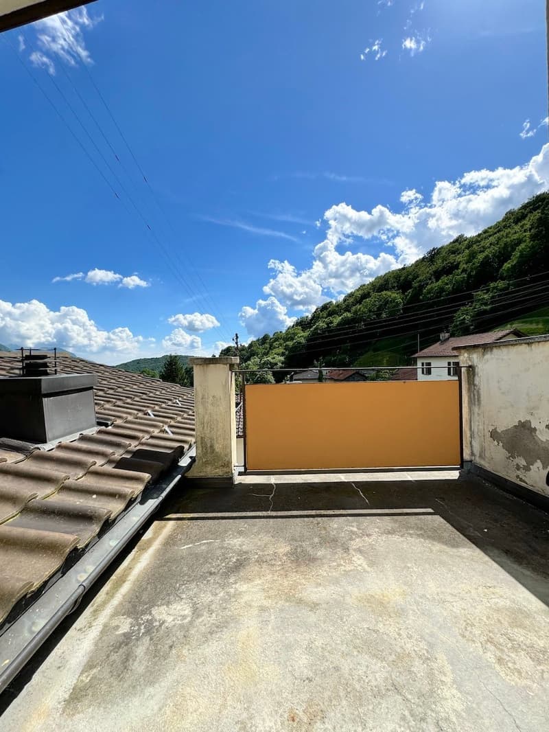 Rooftop area with clear blue sky, large sliding gate, green hills in the background, tiled roof.
