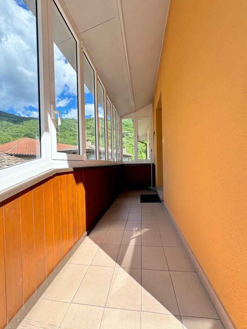 Tiled hallway with view of a balcony with three windows, tiled floor, wooden paneling