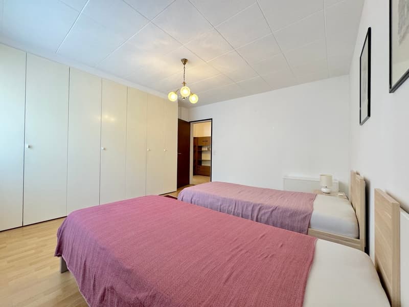bedroom with 2 single beds, white cabinets, wooden floors, white walls, pendant light