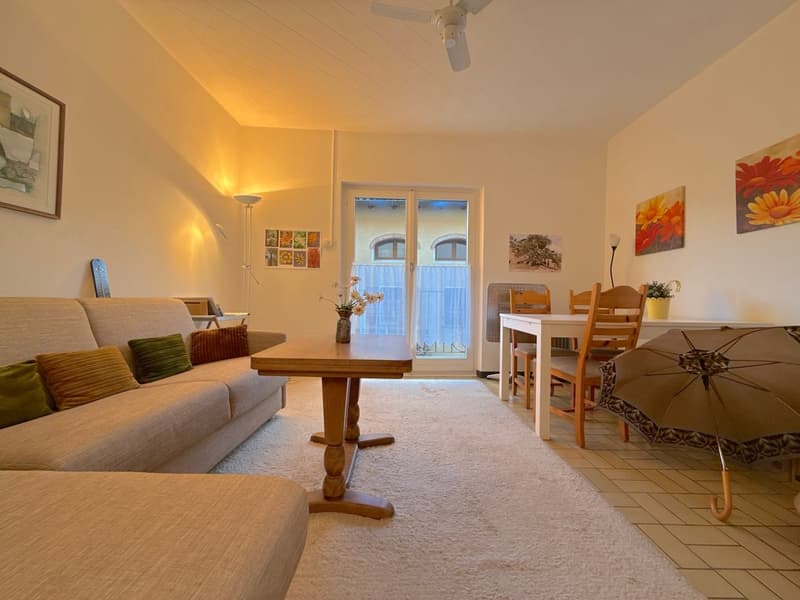 living room with beige couch, table, wooden dining table, dining chairs, floor lamp, paintings on the wall, closed glass door, umbrella, white carpet