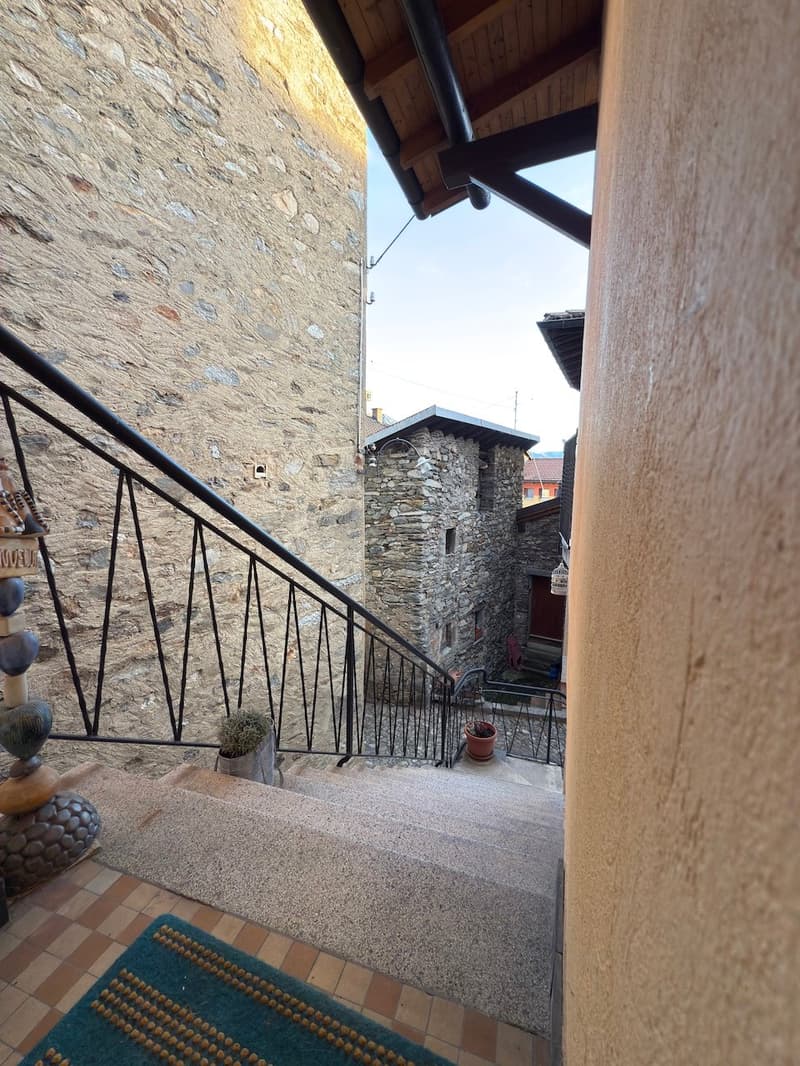 Outdoor staircase leading to an upper level with stone walls and a roof, next to a building entrance.