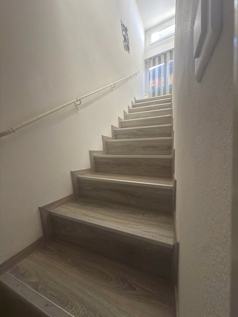 Wooden staircase with silver railing and white painted walls.