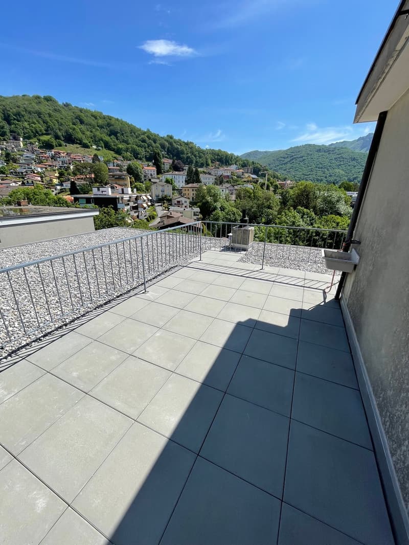 Roof terrace with gray tiles, steel railings, a small washbasin, and a beautiful town and mountain view.