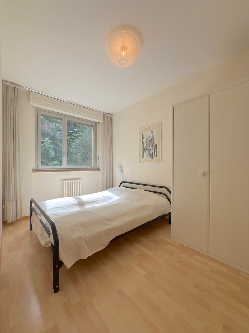 bedroom with a bed, lamp, window with view to the outside, wardrobe, painting on the wall