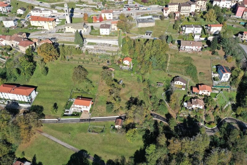 Aerial view of a small village with several houses, a grassy field, and trees.