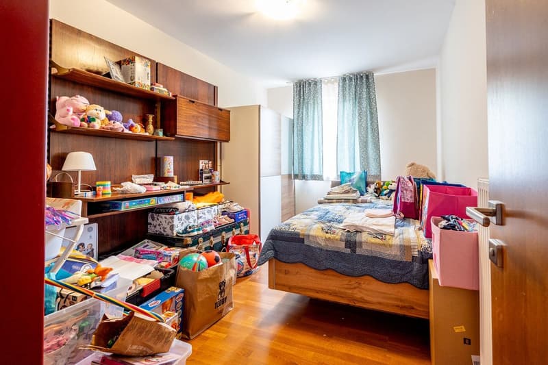 bedroom with bed, wooden shelves, toys, storage boxes, lamp, window with curtains