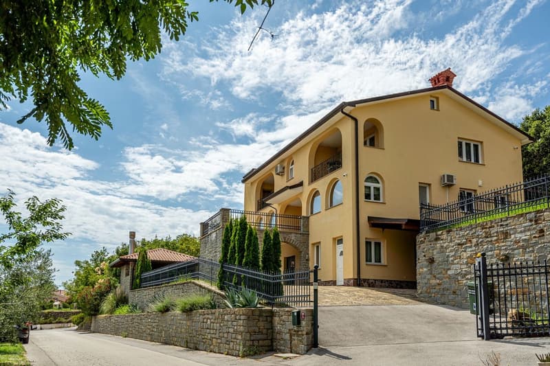2 story house, yellow exterior, stone wall, black fence, balcony, driveway