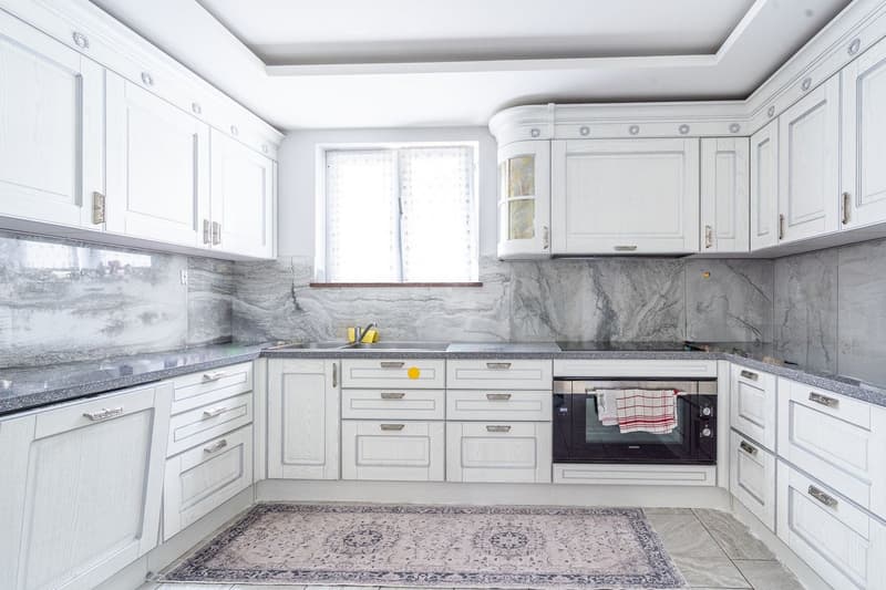 modern kitchen with white cabinets, granite countertops, stainless steel sink, built-in oven, window with white curtains