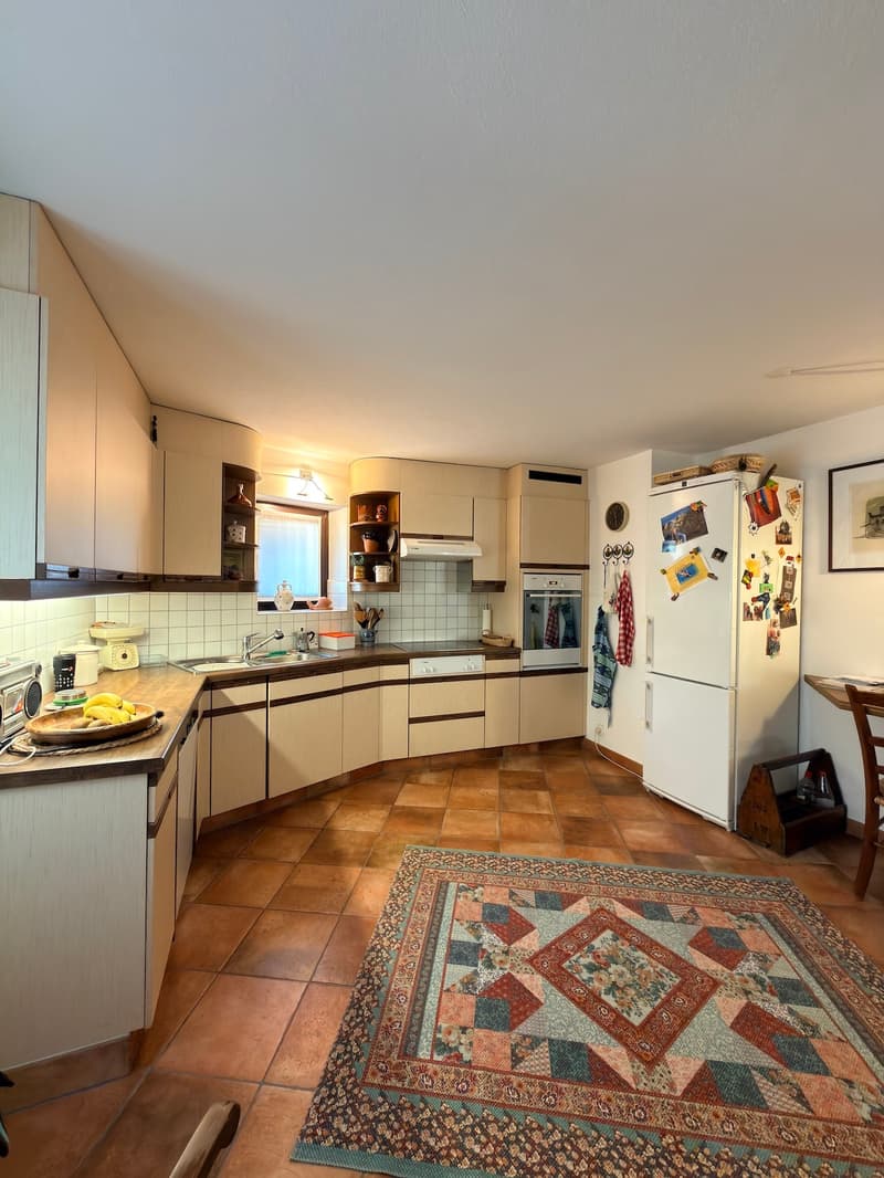 kitchen with wooden cabinets, tiled floor, white refrigerator, sink, oven, countertop with fruits, rug