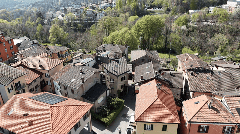 Cluster of houses, red roofs, solar panels, surrounded by trees and greenery