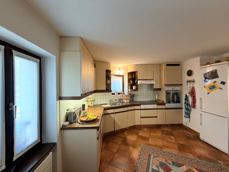 kitchen with wooden cabinets, tiled floor, white appliances, window, sink, countertop with fruits, rug
