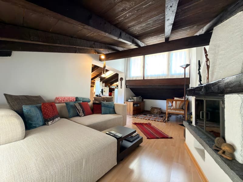 L-shaped sofa, coffee table, fireplace, wooden floor, wooden beams, windows, rug, side table, lamp, wooden cabinet, decorative items