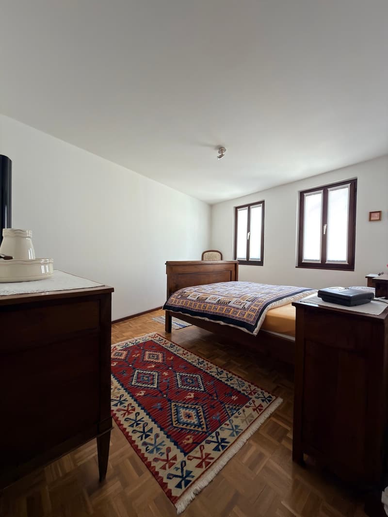 bedroom with bed, rug, wooden furniture, two windows, ceiling lamp