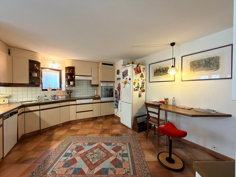 modern kitchen with white cabinets, tiled floor, white refrigerator, wooden table, red stool, two framed pictures on the wall
