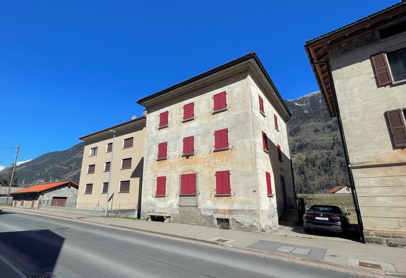 Large building with red shutters, several windows, steep slope roof, small car parked in front of the building