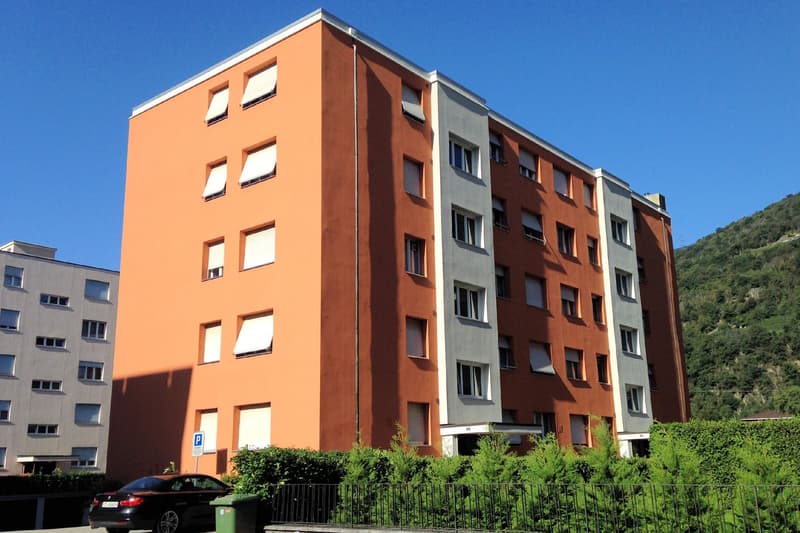 modern apartment building, orange exterior, white windows, fenced garden, mountain view