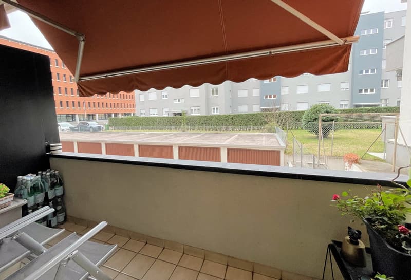 balcony, tiled floor, chairs, potted plants, canopy, view of a building and a parking lot