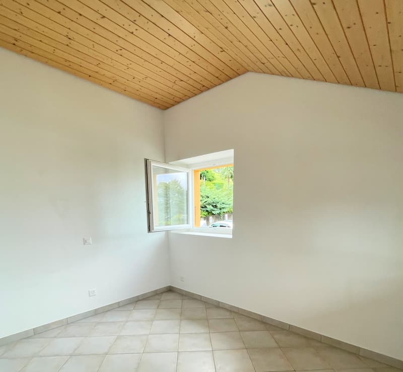 Small room, white walls, tiled floor, small window with white frame and view of outside greenery.