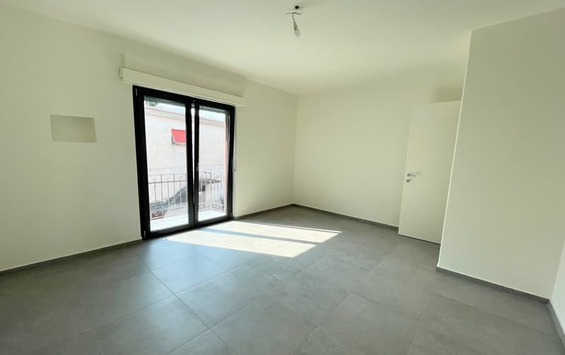 large open room, white walls, gray tiles, sliding glass door to balcony, no furniture