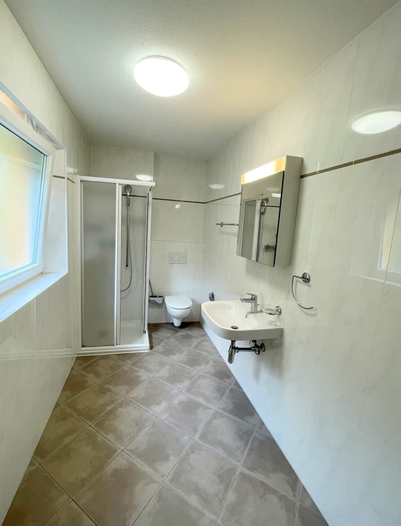 white bathroom with a glass shower, white ceramic sink, mirror, white toilet, tiled floor, small window