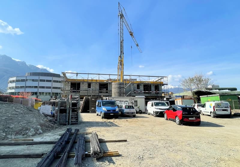 construction site with a crane, white vans, scattered construction materials, distant buildings, mountainous background