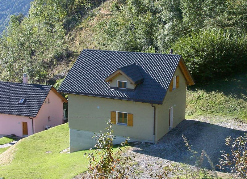 Single-story house, beige exterior, grey tiled roof, chimney, large windows, wooden door, gravel driveway, adjacent smaller pink house
