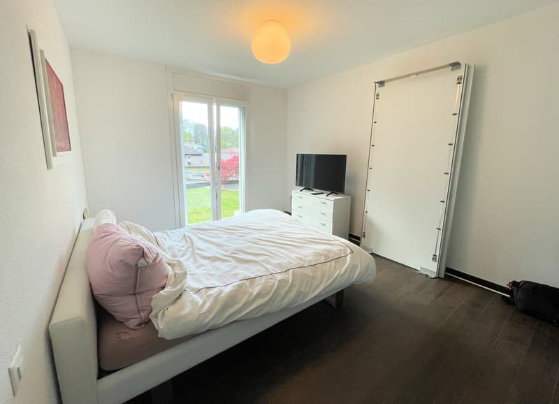 white walls, wooden floor, bed, TV, sliding glass door leading to balcony