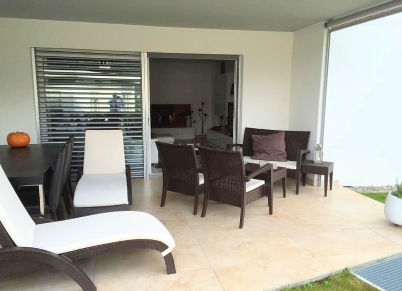 Patio with wicker furniture, tile flooring, pumpkin on table, plants and shrubs