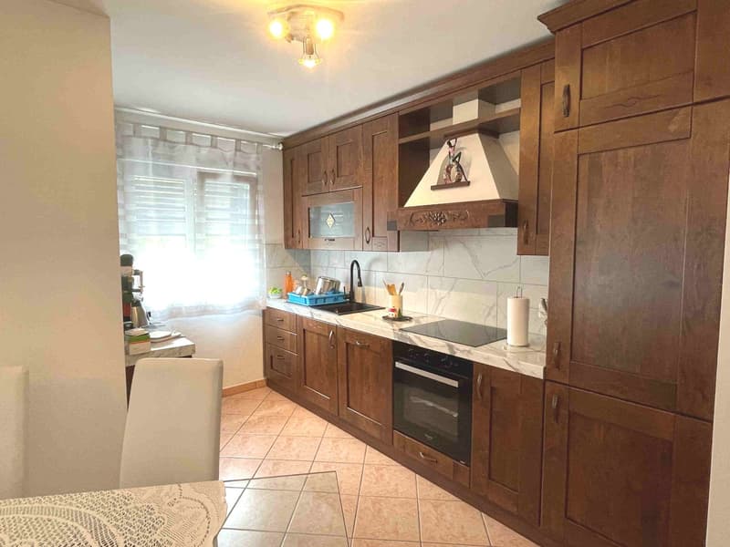 wooden cabinets, marble countertops, built-in oven and stove, sink with faucet, ceiling light, white tiled floor