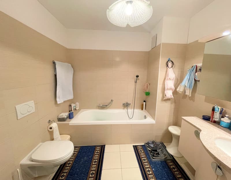 Modern bathroom with a bathtub, shower, toilet, sink, and tiled flooring, along with various toiletries.