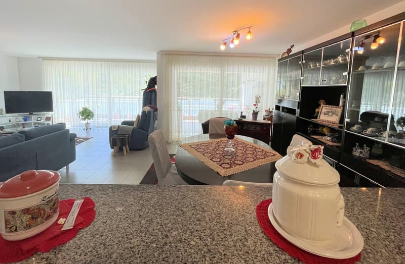 Living room with couch, dining table, dining chairs, television, glass cabinets, table cloth, and balcony