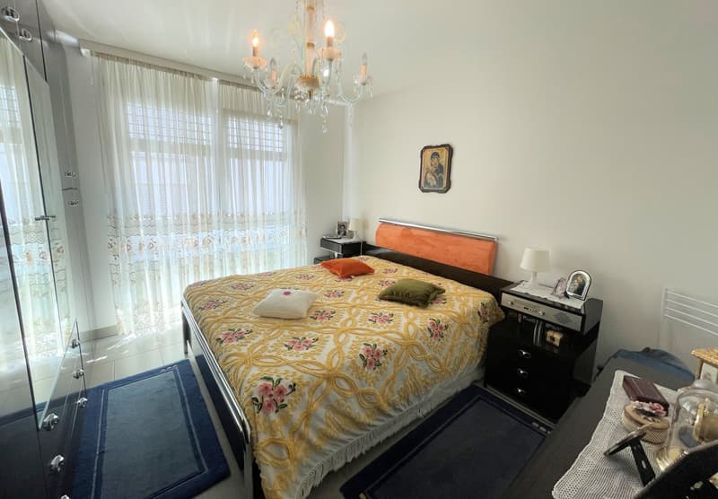 double bed with floral coverlet, two nightstands with lamps, chandelier, picture frame, blue carpets, glass window with curtains
